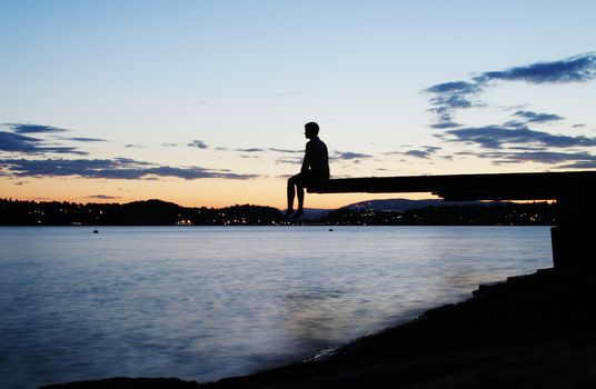 A young person sitting on a dock at dusk, at the fjord in Oslo, Norway