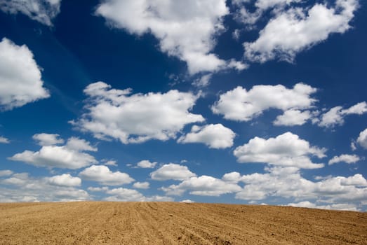 Blue sky with clouds over ploughed field.