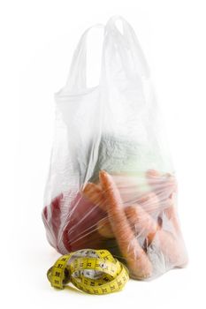 Healthy vegetables in a clear plastic grocery bag on a white background with a tape measure in the foreground