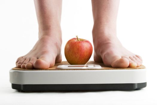 A pair of female legs standing on a bathroom scale with an apple between them.