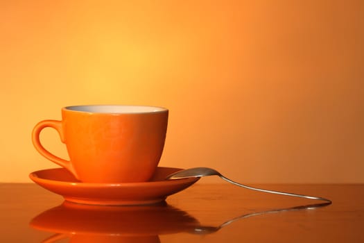 Nice red cup on saucer with spoon isolated on gradient ginger background