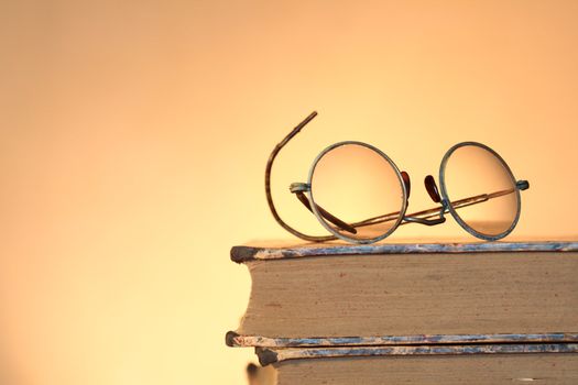 Old spectacles lying on ancient books isolated on yellow background