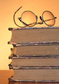 Old spectacles lying on ancient books isolated on yellow background