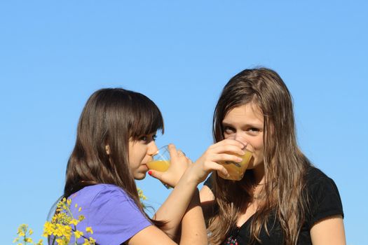 Two beauty teenage girls drinking orange juice against the blue sky