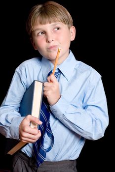 A school boy student in uniform holding textbook and pencil and thinking.  Dark background.