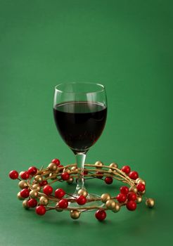 glass of red wine with xmas ornament, green background