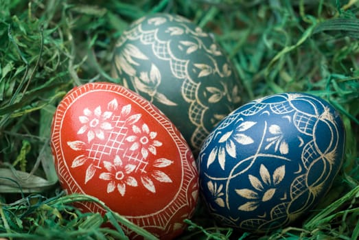 Three handmade easter eggs on the green hay. Selective focus, shallow depth of field.