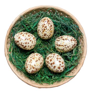Basket with spotted eggs on the green hay. Clipping path included.