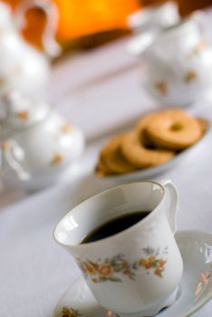 Coffee set on the table - cup of coffee on the front (shallow DOF focus on the liquid edge) cookies and milk jug, sugar bowl behind.