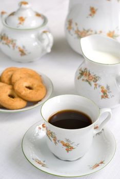 Coffee (or tea) set on the table - cup of coffee on the front (focus on it) cookies, milk jug and sugar bowl behind.