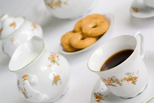 Coffee (or tea) set on the table - cup of coffee on the front (focus on it) cookies, milk jug and sugar bowl behind. Shallow depth of field.