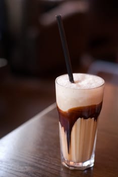 Latte macchiato coffee with chocolate decoration and straw (focus on the froth surface) on the cafe table. Shallow depth of field.