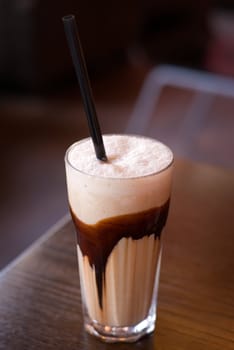 Latte macchiato coffee with chocolate decoration and straw (focus on the froth surface) on the cafe table. Shallow depth of field.