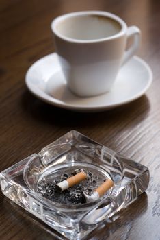 Ashtray and empty coffee cup on the cafe table. Shallow depth of field (focus on the cigarette butt).