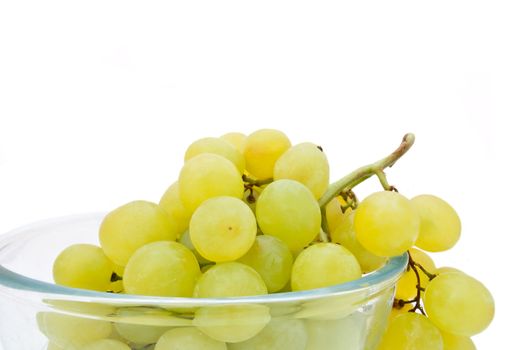 Close and low level capturing a glass bowl containing fresh green grapes arranged over white.