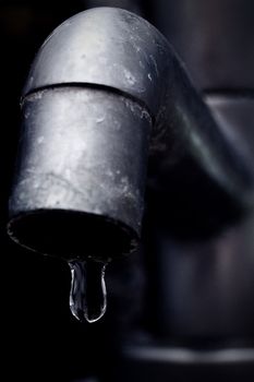 An old leaky faucet with a drop of water, meaning the waste of water in the world.
