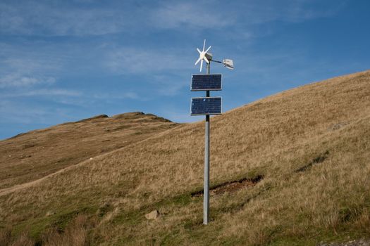 Wind turbine and solar panel combination on mountain side.