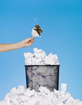 Hand holding a piece of paper in flames over a wastebasket
