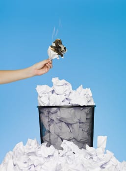 Hand holding a piece of paper in flames over a wastebasket