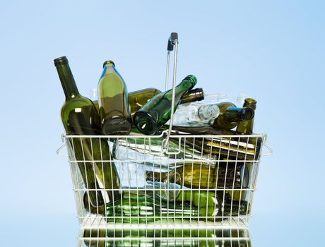 Empty glass bottles in a wastebasket on blue background