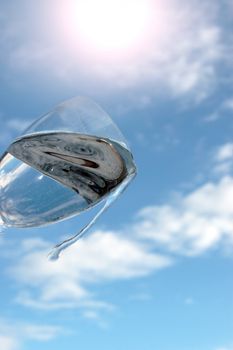 a glass of water being poured against a bright sunny cloudy blue sky background