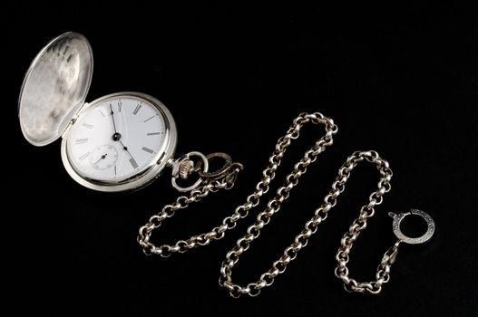 Elegant carved silver pocket watch with chain isolated on black