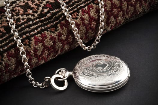 Elegant carved silver closed pocket watch with chain over a carpet