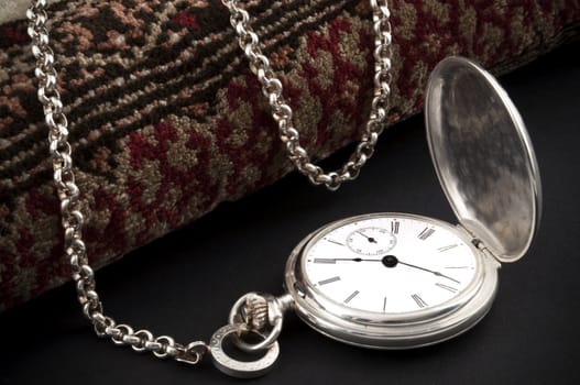 Elegant silver pocket watch over a rolled carpet