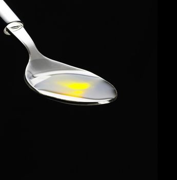 olive oil poured on a spoon over black background