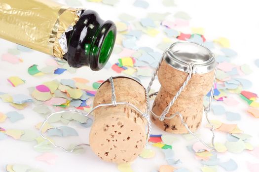 Empty champagne bottle, two corks and confetti on white background