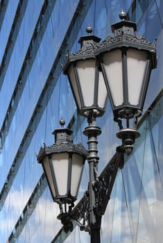 Old street lamp in front of modern buildings.