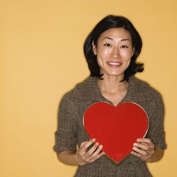 Pretty mid adult Asian woman holding red heart shaped box.