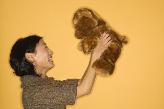 Pretty Asian mid adult woman holding brown teddy bear and smiling.