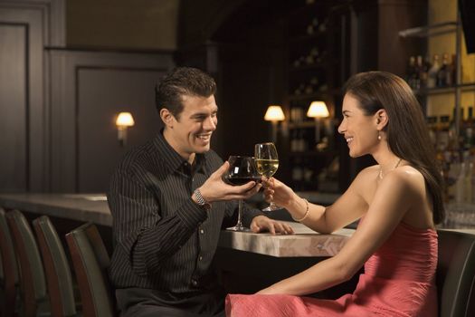 Mid adult Caucasian couple at bar toasting wine glasses and smiling.