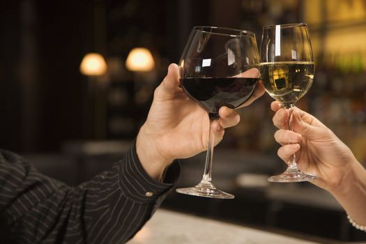 Mid adult Caucasian male and female hands toasting wine glasses.