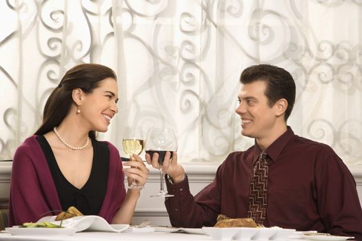 Mid adult Caucasian couple smiling and toasting wine glasses in restaurant.