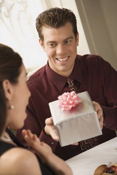 Mid adult Caucasian man presenting wrapped gift to surprised woman at restaurant.