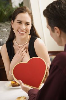 Mid adult Caucasian man giving a heart shaped box of chocolates to woman at restaurant.