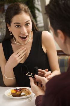 Mid adult Caucasian man proposing marriage to surprised woman at a restaurant.