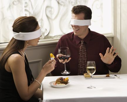 Mid adult Caucasian couple dining in a restaurant with blindfolds over eyes.