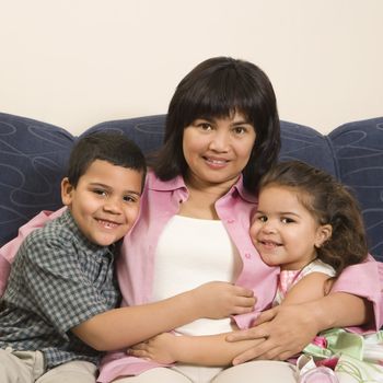 Family sitting on couch hugging each other smiling and looking at viewer.