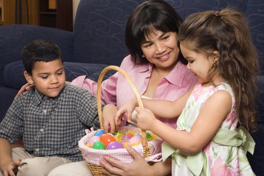 Hispanic mother with her boy and girl at home looking through Easter basket.