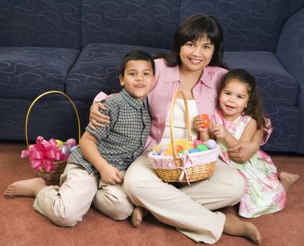 Family sitting on floor with Easter baskets smiling and looking at viewer.