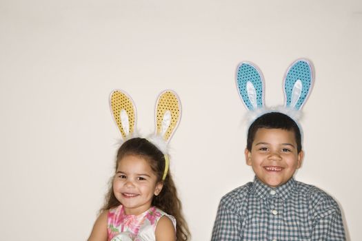 Hispanic boy and girl wearing bunny ears smiling and looking at viewer.