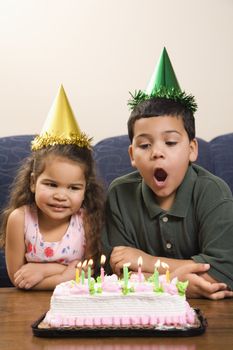 Hispanic girl and boy wearing party hats preparing to blow candles out on birthday cake.