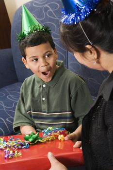 Mother giving present to surprised son at birthday party.