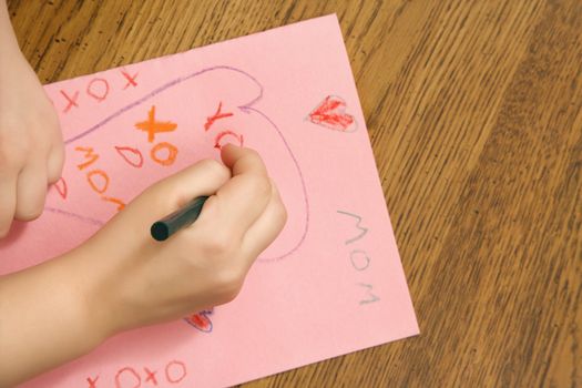 Caucasian female child hands drawing on paper with crayons.