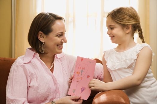 Caucasian girl giving mid adult mother a drawing.