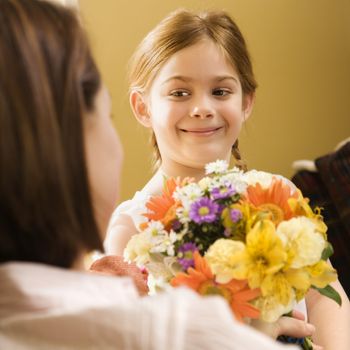 Caucasian girl giving mid adult mother flowers.