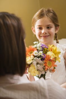 Caucasian girl giving mid adult mother flowers.